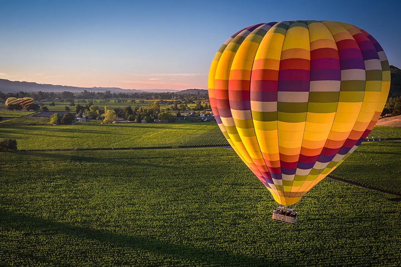 A striped hot air balloon coming down over a vineyard in Napa Valley