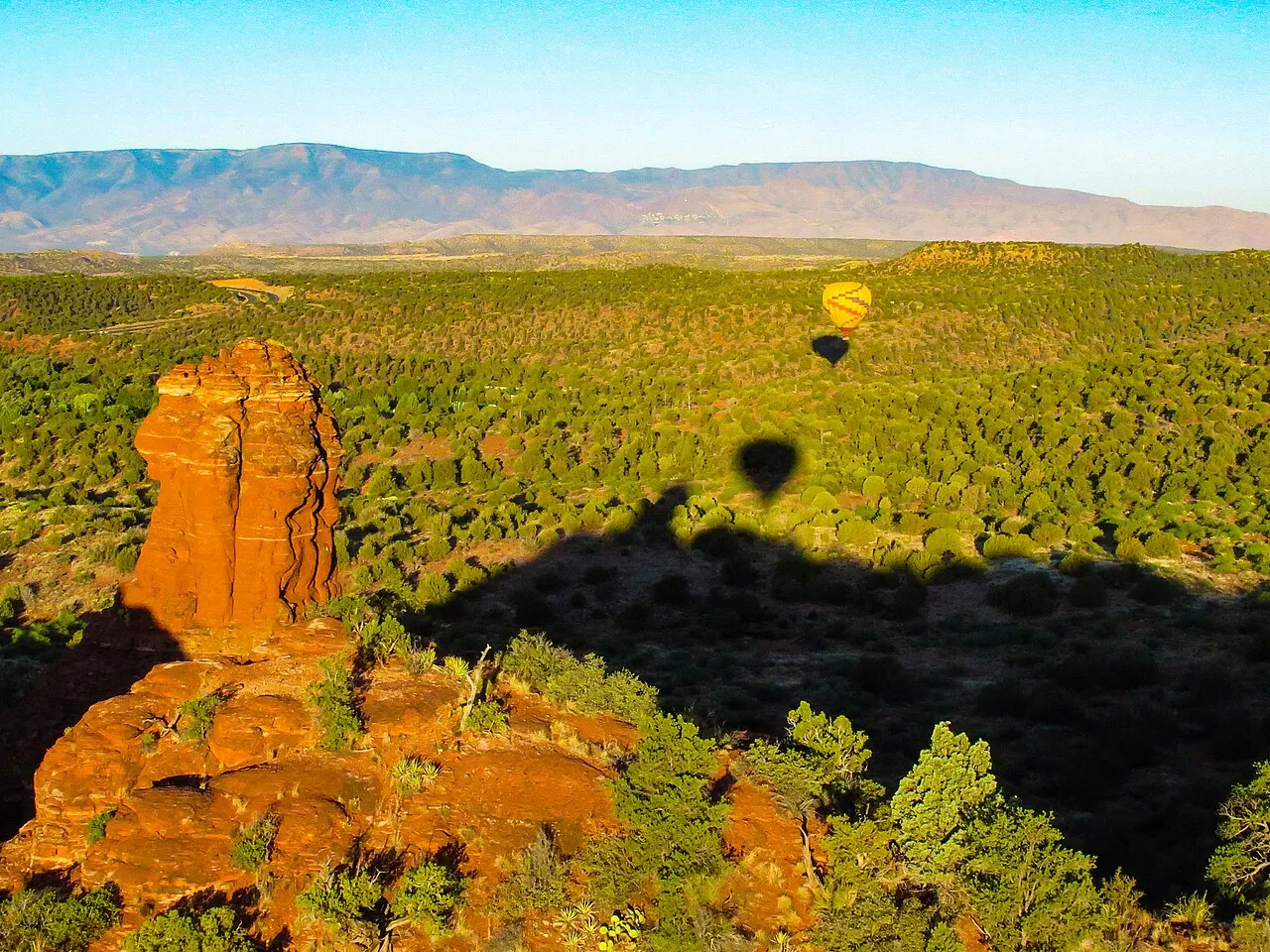 A hot air balloon and its shadow above the red rocks near Sedona